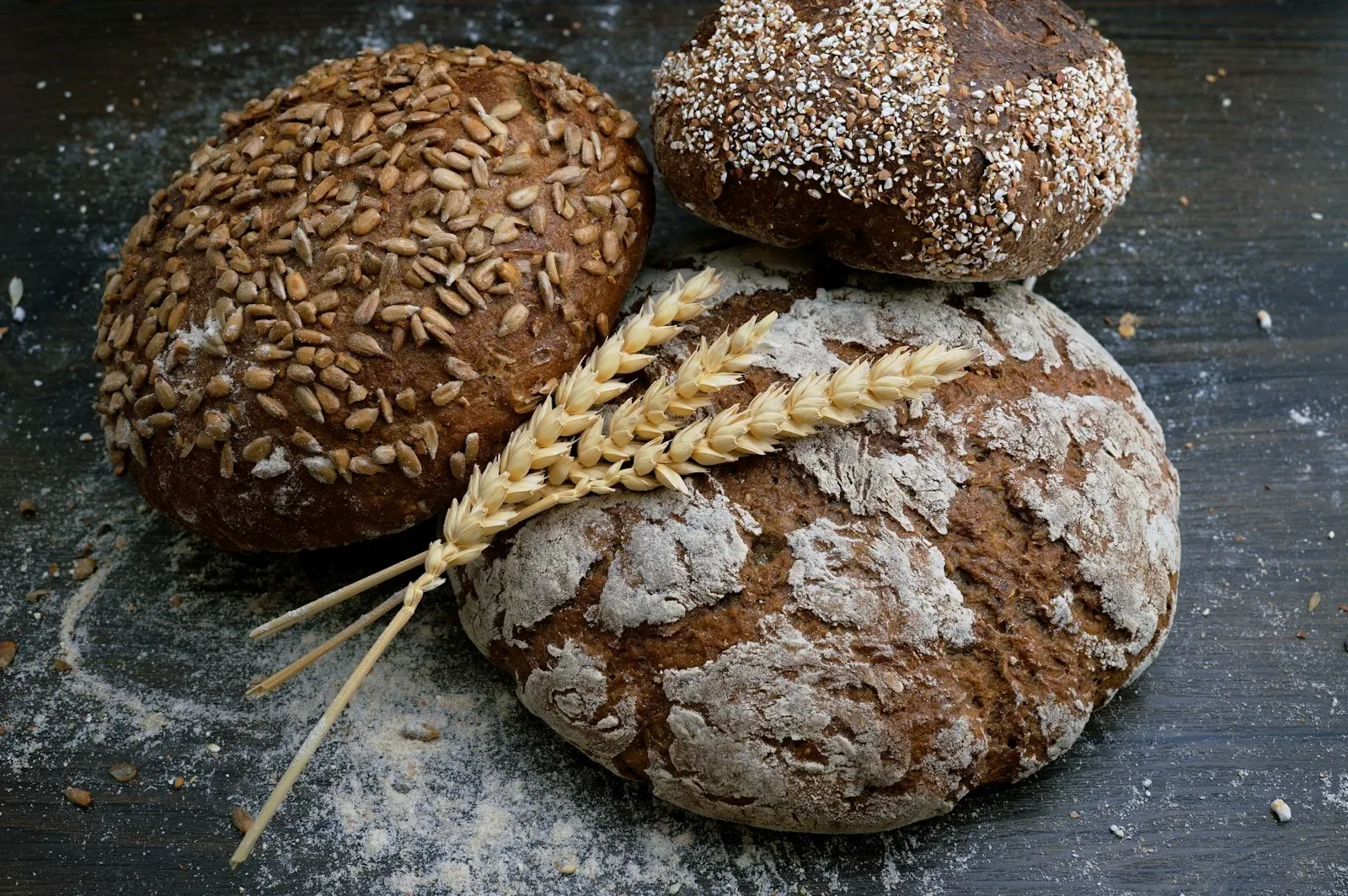 Seeded rye and sourdough loaves with ears of wheat on a dark counter