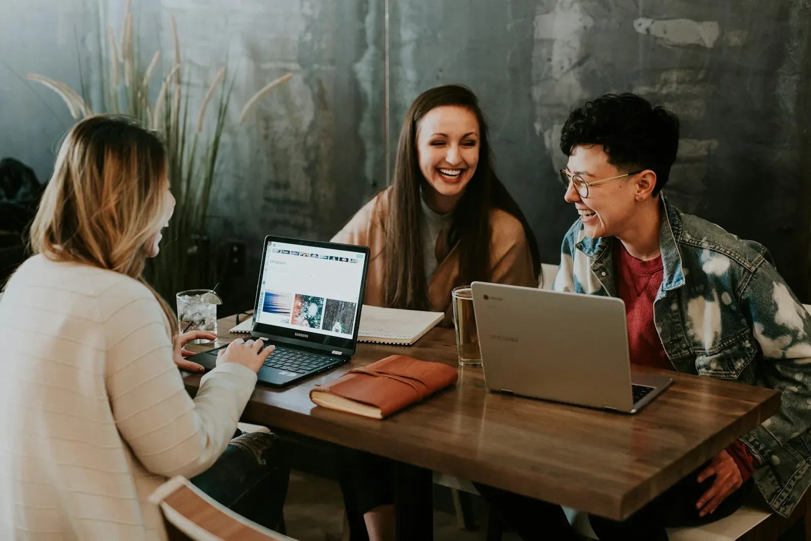 Three people looking at a laptop together across a café table